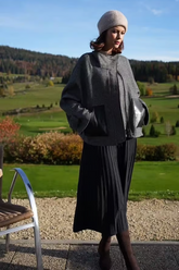 a lady in a grey wool jacket and a black pleated skirt